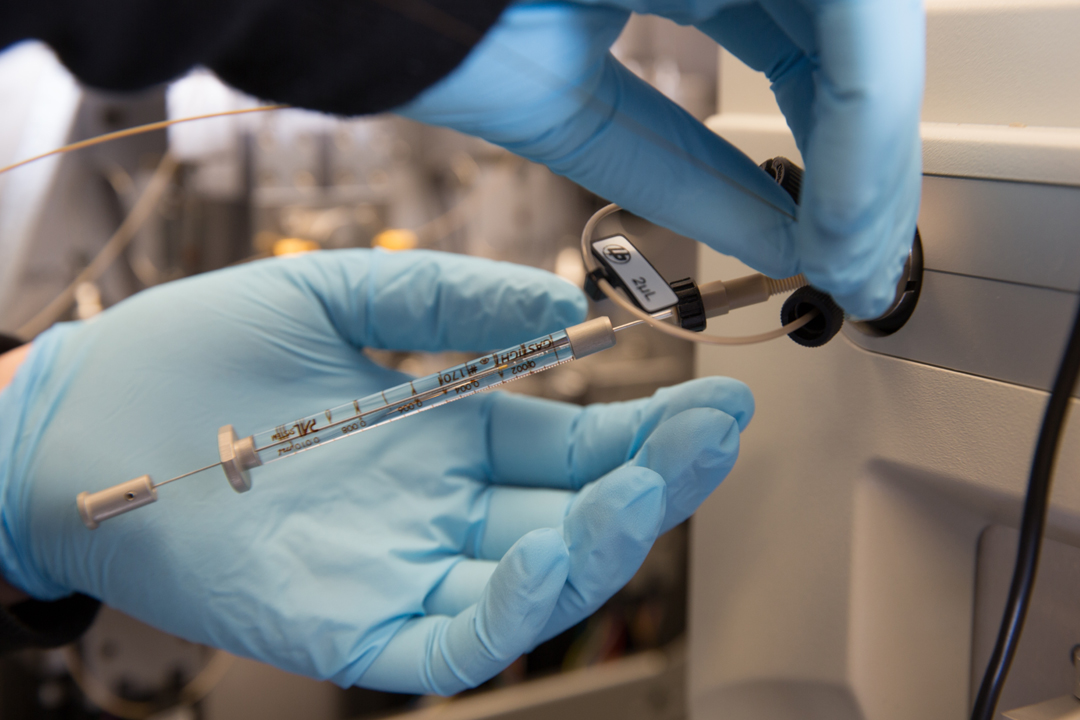 gloved hands inserting needle into a machine